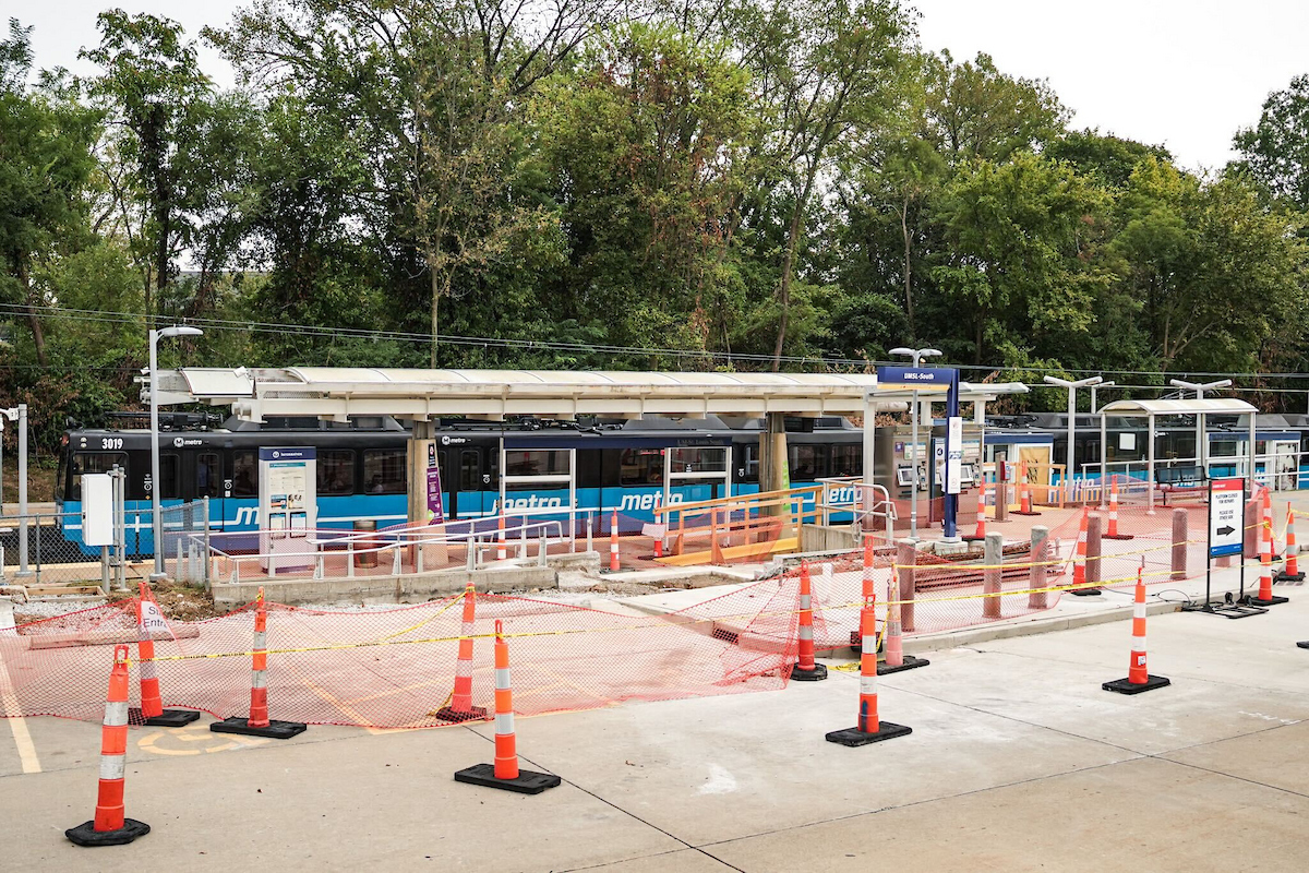 UMSL South Station with construction in the foreground and a train passing through the station in the background